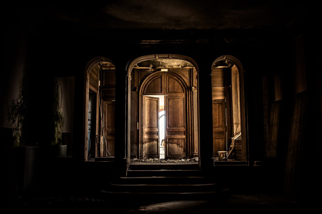 urbex grande porte en bois majestueuses entrouvertes la lumière filtre depuis l'entrebaillement de la porte