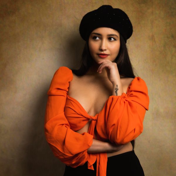 portrait studio jeune femem latino habillée en orange te noir avec un beret noir