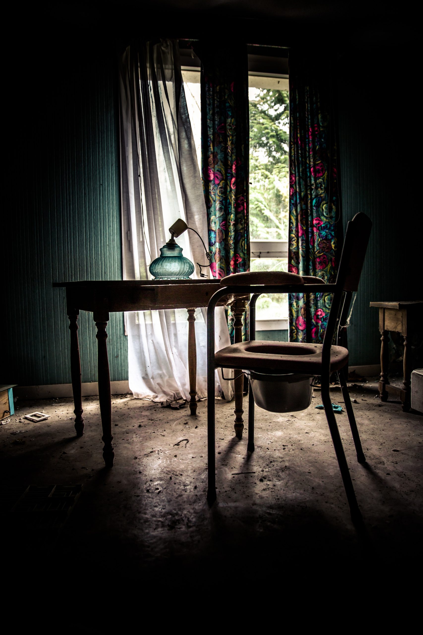 urbex contre jour d'un bureau avec chaise en bois devant une fenetre bel abas-jour en verre vert posé sur la table avec la lumière qui le traverse