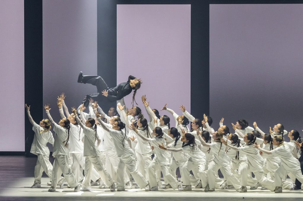 spectacle de danse sur scène, un groupe de danseurs en blanc au sol soulève une danseuse en noir qui les surplombe